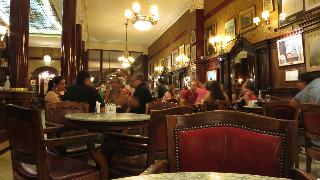 Das elegante Interieur eines Cafés mit Holzvertäfelung und Kronleuchtern, in dem Gäste von Personal bedient werden.